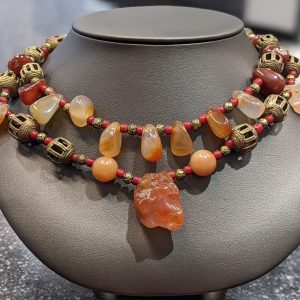 HARD STONE BEADED NECKLACE WITH RED AND ORANGE HUES AS WELL AS LANTERN SHAPED AND SMALL ROUND METAL PIECES IN BETWEEN. EARRINGS TO MATCH.
