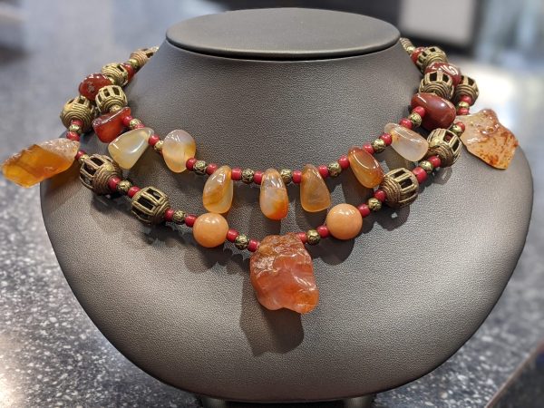 HARD STONE BEADED NECKLACE WITH RED AND ORANGE HUES AS WELL AS LANTERN SHAPED AND SMALL ROUND METAL PIECES IN BETWEEN. EARRINGS TO MATCH.